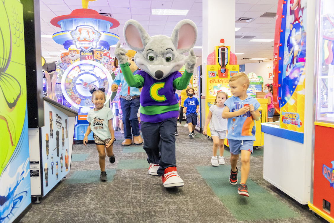 This photo shows two children running along with Chuck E. Cheese in one of the brand's restaurants.