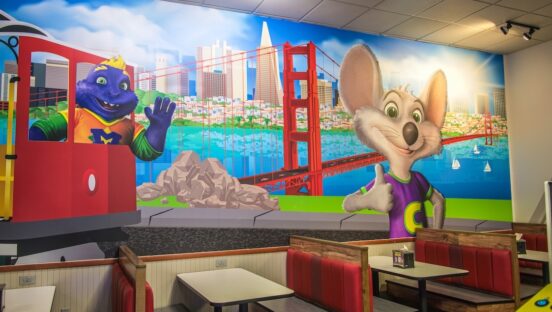 This photo shows the interior of a Chuck E. Cheese with a mural showing the animated mascot and other characters.