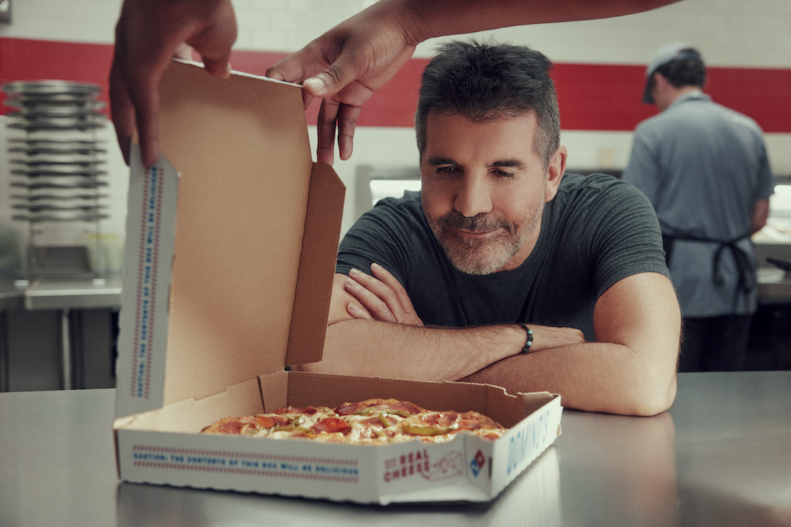 This photo shows Simon Cowell grinning and staring at a pizza in a box.