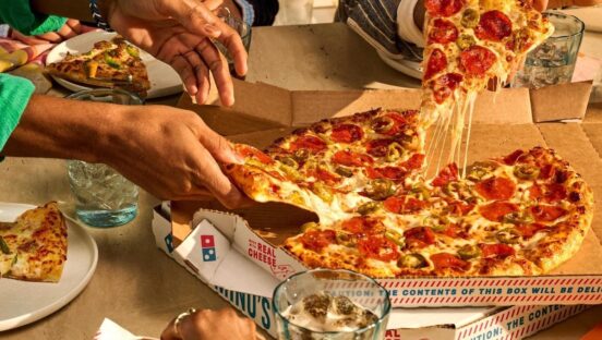 Hands reach for Domino's pizza on a crowded table.