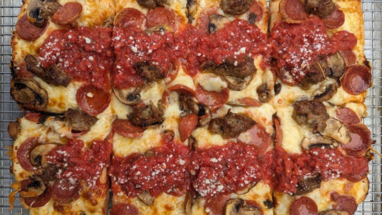 This photo shows a Detroit-style pizza topped with pepperoni, sausage and mushrooms.