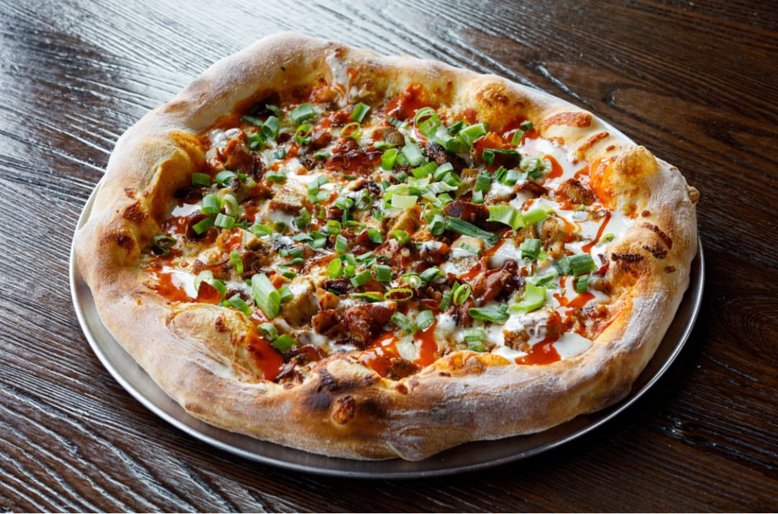 This photo shows a pizza topped with Buffalo chicken and other ingredients.