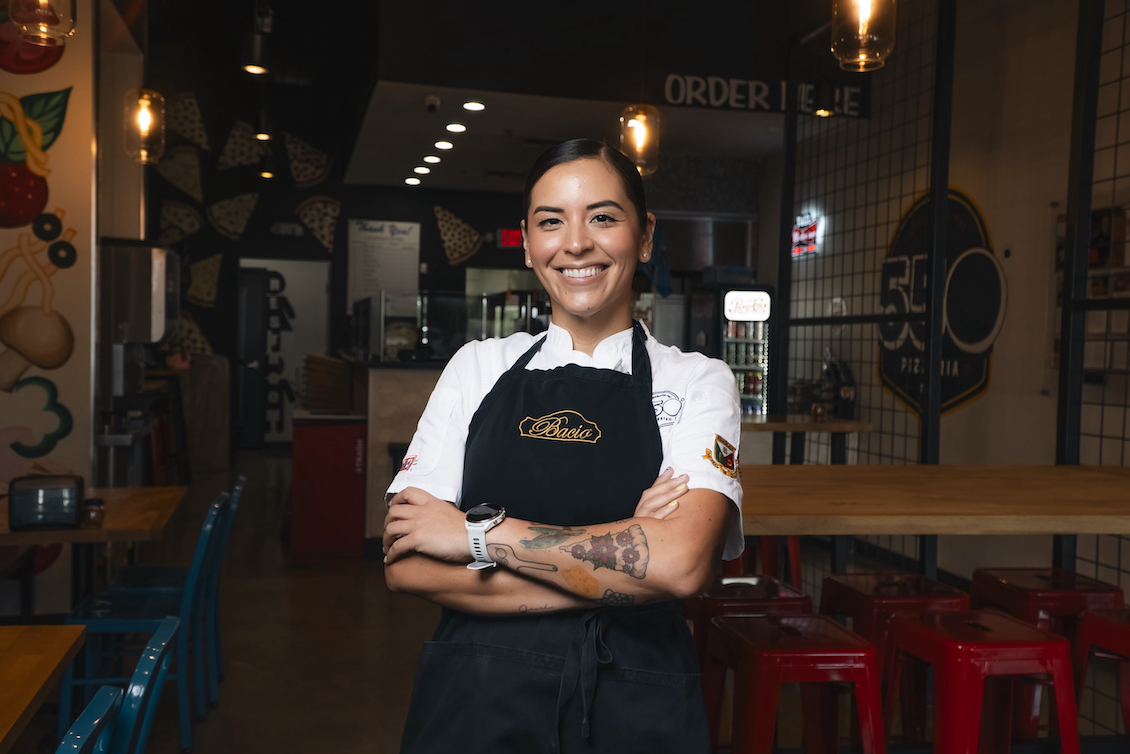 This photo shows Janet Zapata smiling with her arms crossed. She's wearing a black apron over a dressy white shirt.