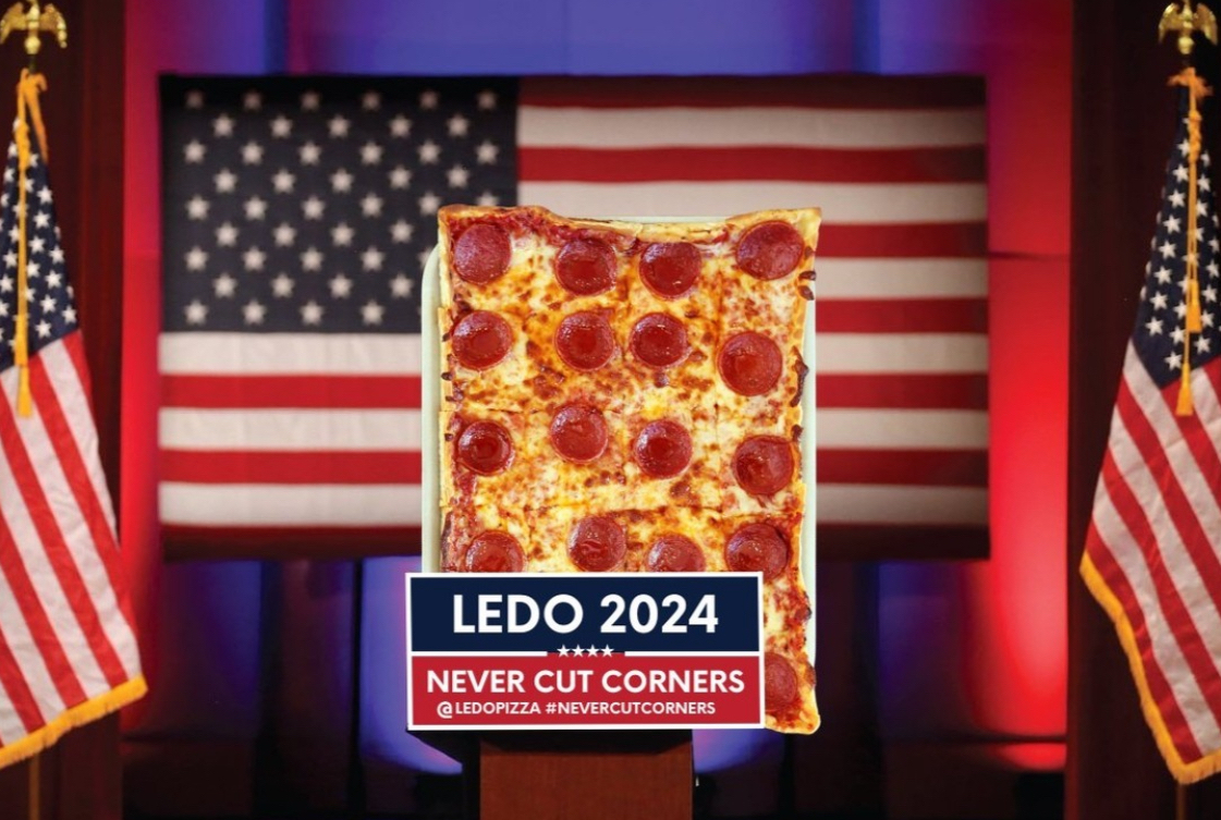 This photo shows a Ledo pepperoni pizza flanked by U.S. flags and a banner that reads, "Ledo 2024: Never Cut Corners."