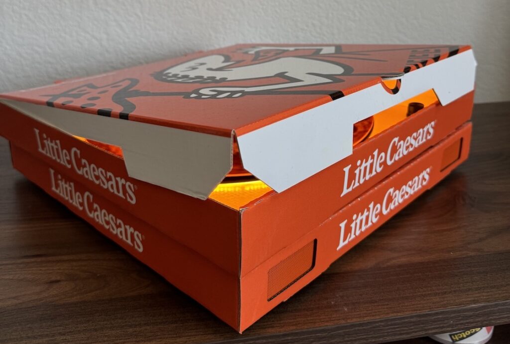 This photo shows a Little Caesars pizza box slightly opened with a bright orange light shining inside.
