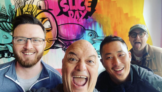 Lee Kindell, owner of MOTO Pizza in Seattle, poses with three other men inside one of his storefronts. A graphic on the wall of the restaurant reads "have a slice day."