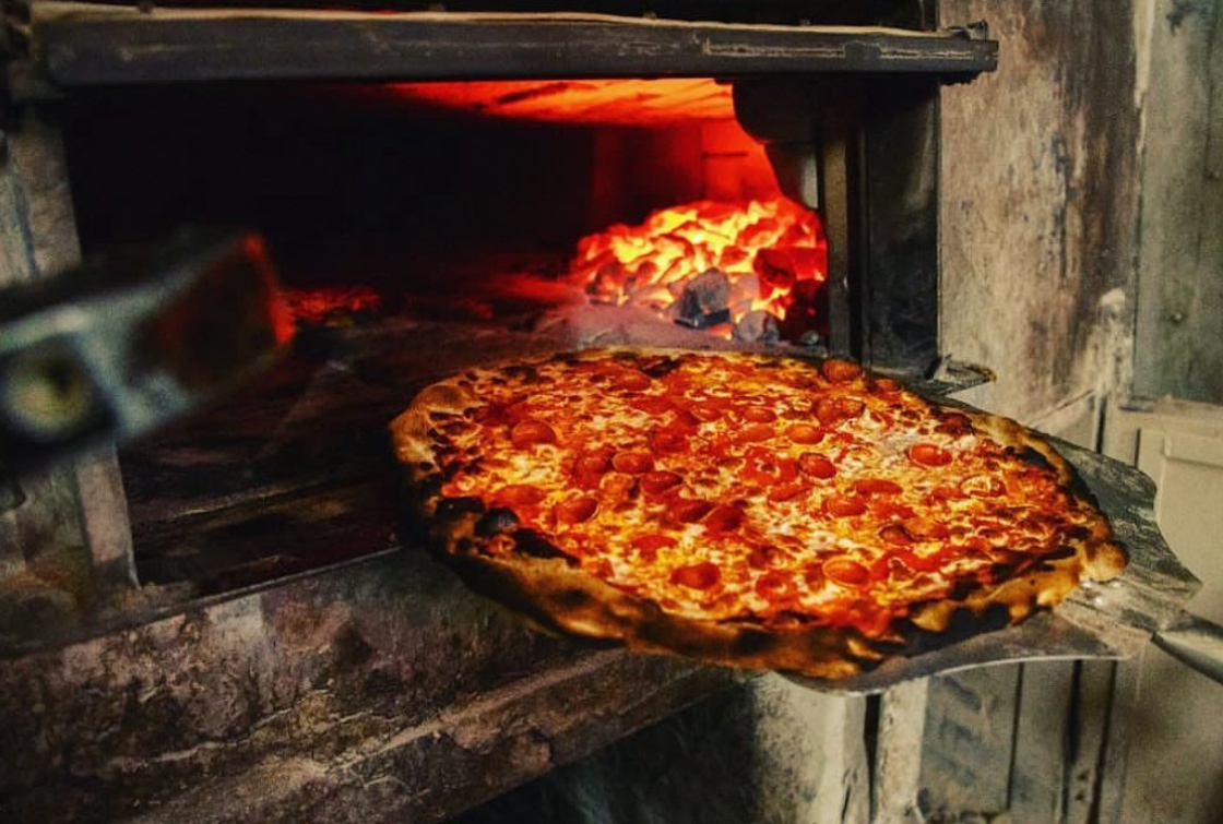 This photo shows a delicious-looking pepperoni pizza, with a nicely blistered crust, coming out of the coal-fired oven at Patsy's Pizzeria.