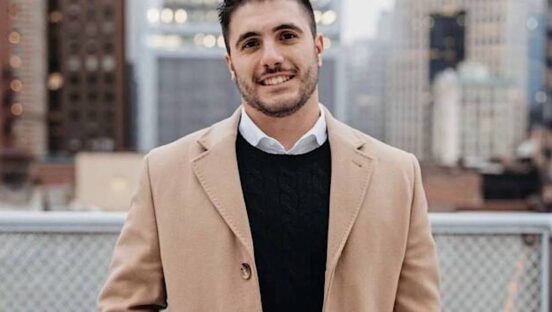 This photo shows the late Domenico Schiano di Cola, smiling, with short, dark hair, wearing a tan sport coat over a dark sweater and white dress shirt.