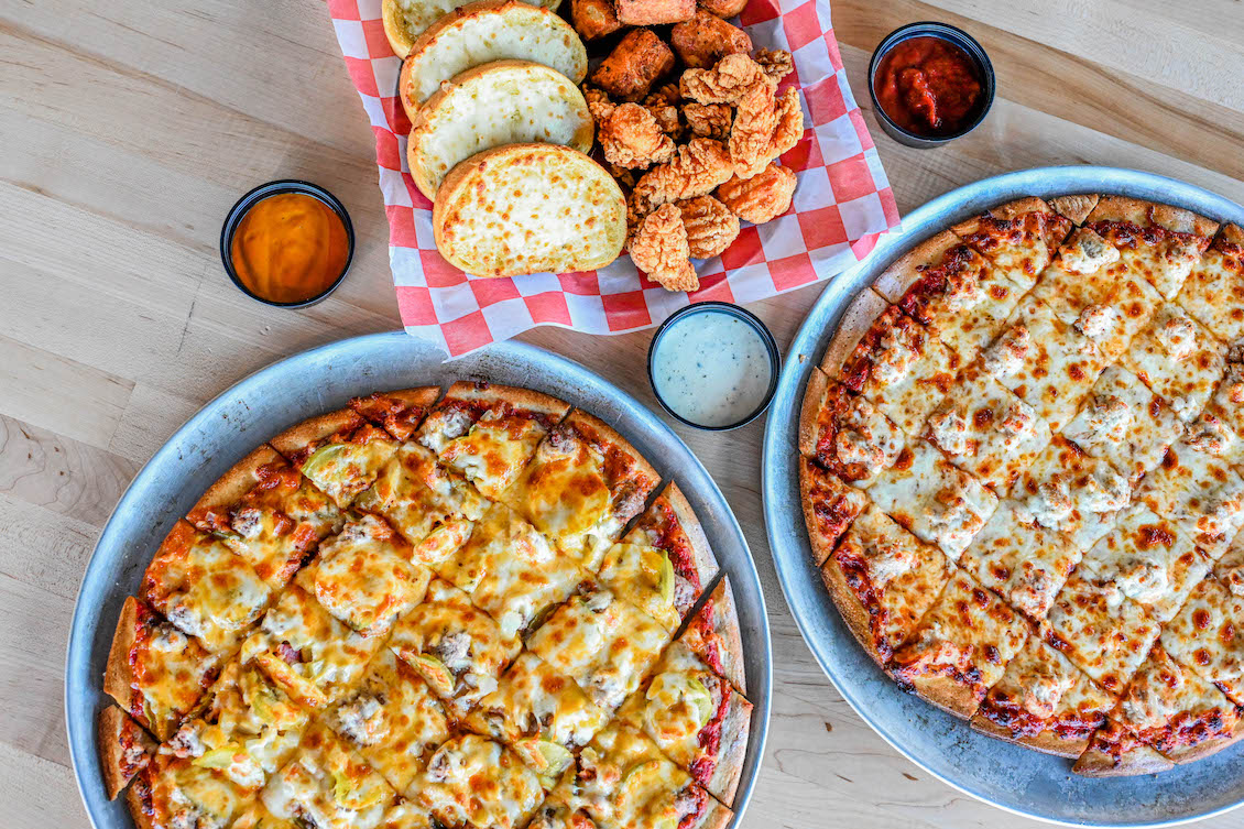 This photo shows a couple of different 'Sota-style pizzas along with bread and other side items.