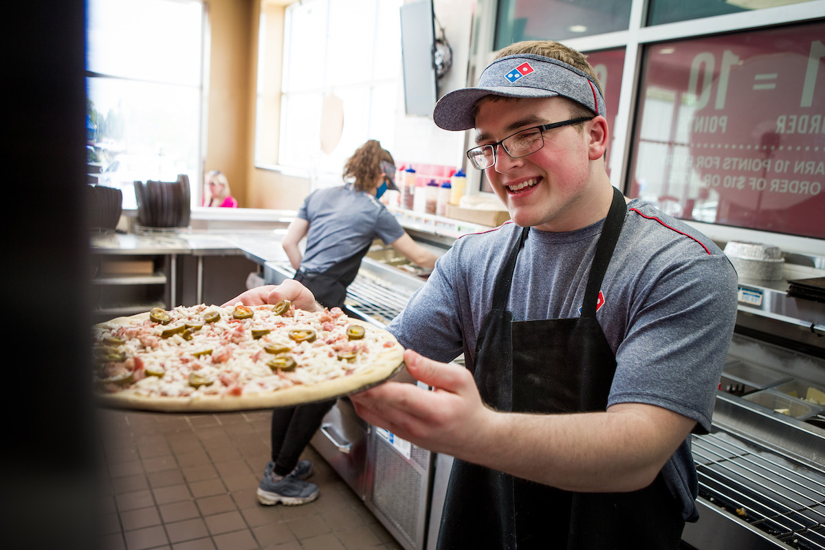 A man makes pizza in a Domino's kitchen.