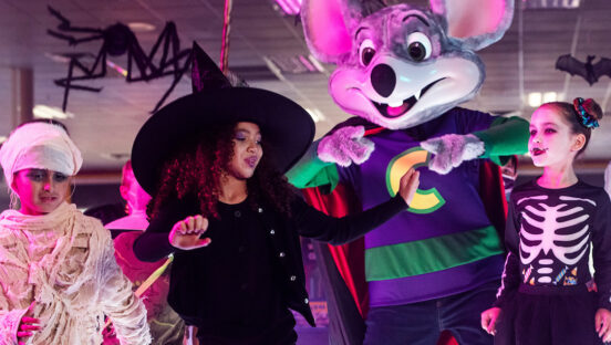 This photo shows Chuck E. Cheese with three kids dressed in Halloween costumes, including a mummy, a witch and a girl in a skeleton costume.