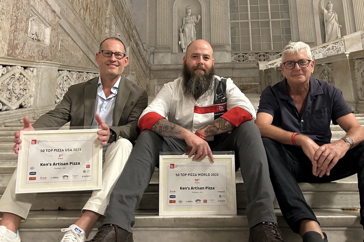 Three men sit on the steps of an Italian building with ancient architecture.