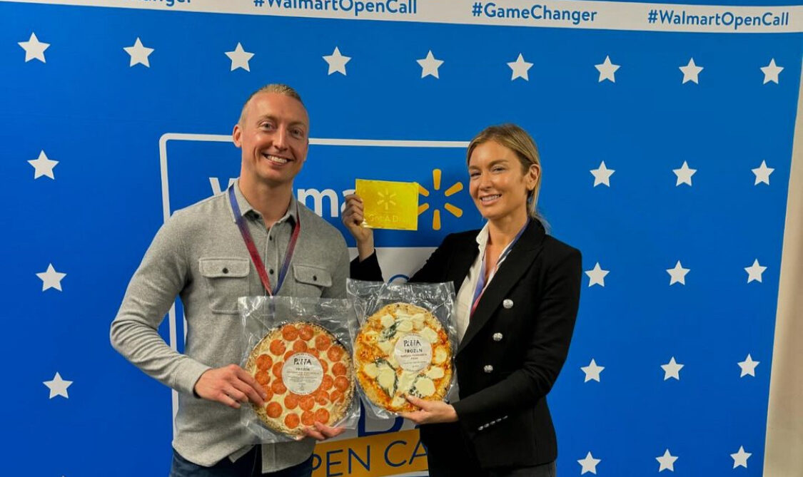 This photo shows Chef Jake Sanderson on the left and Katie Lee on the right. They're both holding a frozen pizza and Katie is displaying her Golden Ticket.
