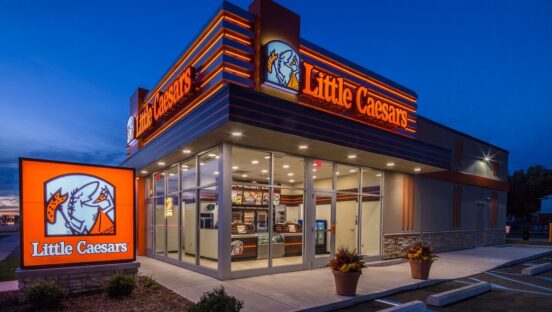 This photo shows the exterior of a Little Caesars story, brightly lit, against a dark blue background.