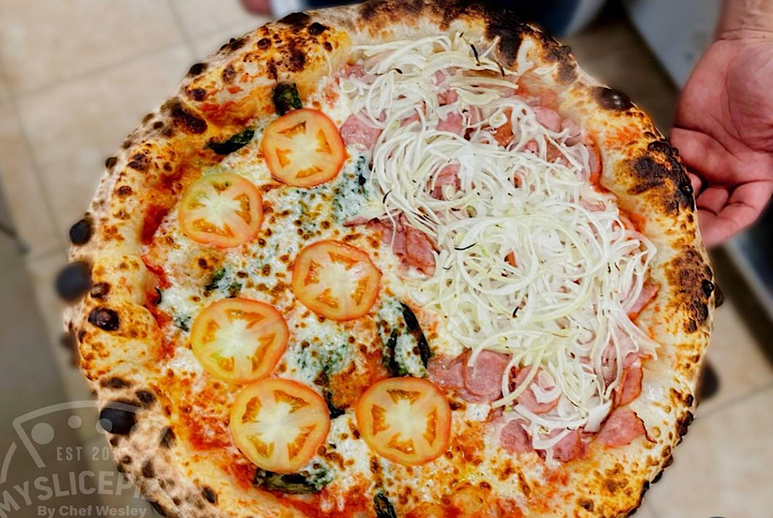 This photo shows a pizza with a beautifully blistered crust topped with sliced onions on one side and tomato slices on the other.