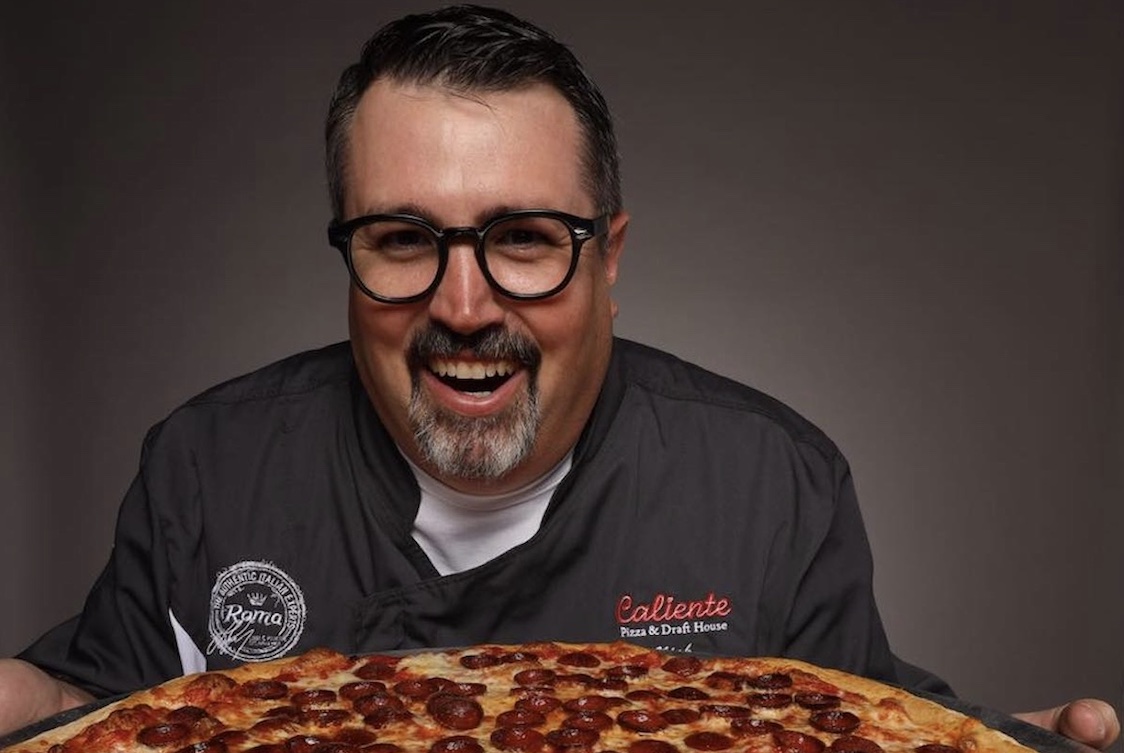 This photo shows a smiling Nick Bogacz, with a goatee and glasses, holding a pizza.