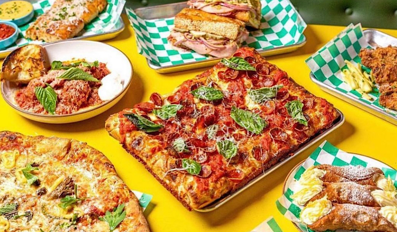 This photo shows a variety of Old Greg's menu items, including a rectangular pepperoni pizza, a round pizza, sandwiches, cannoli and more.