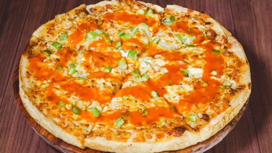This photo shows a pizza topped with topped with blue cheese, chicken, celery and drizzled with buffalo sauce.
