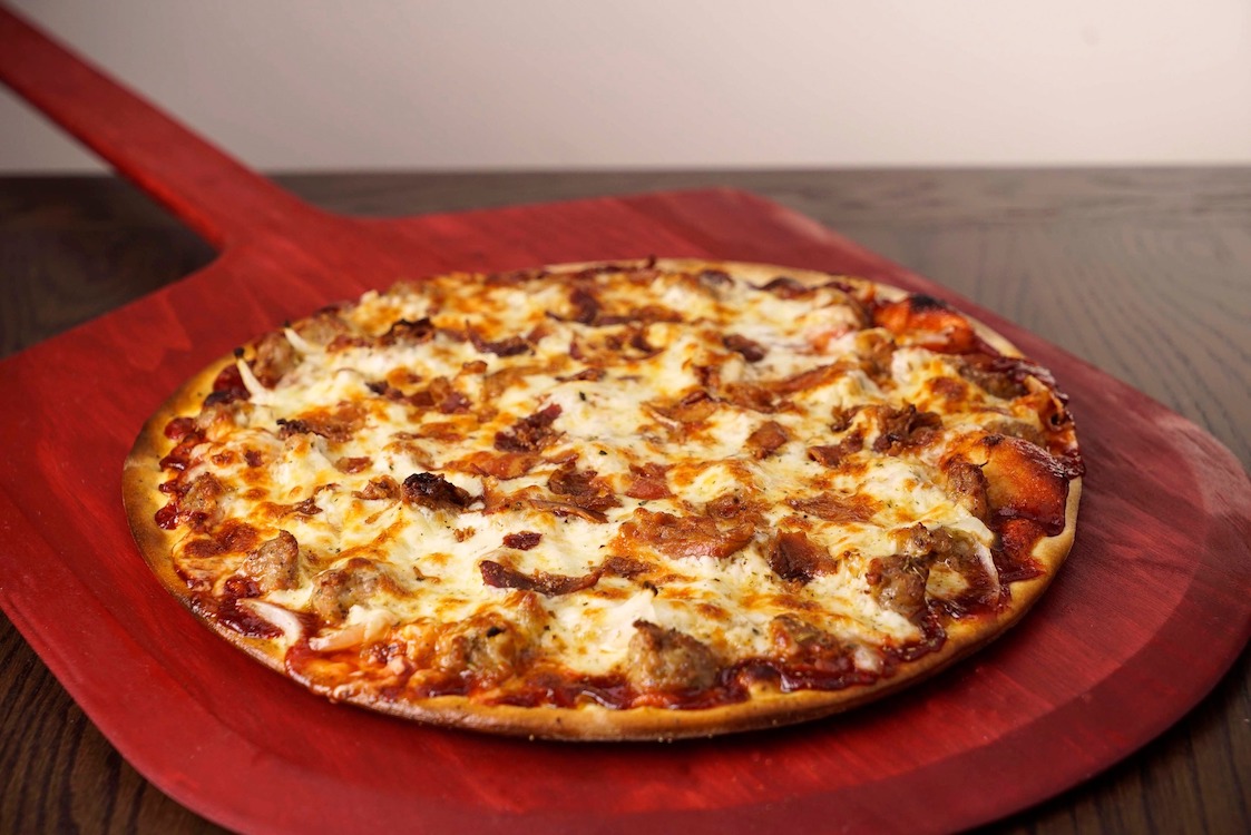 This photo shows a tavern-style pizza topped with sausage, onion, bacon and barbecue sauce.