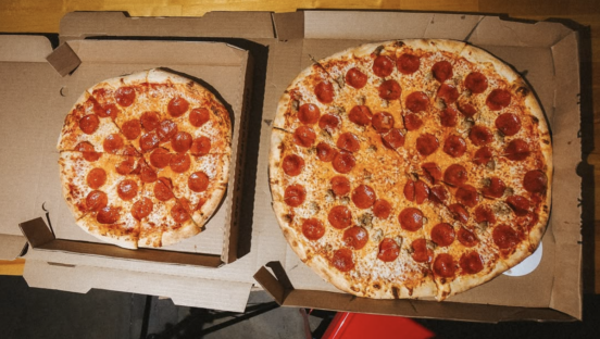Two pepperoni pizzas side by side. The one on the left is a 14" pizza, the one on the right is an 18" pizza and dwarfs the other.