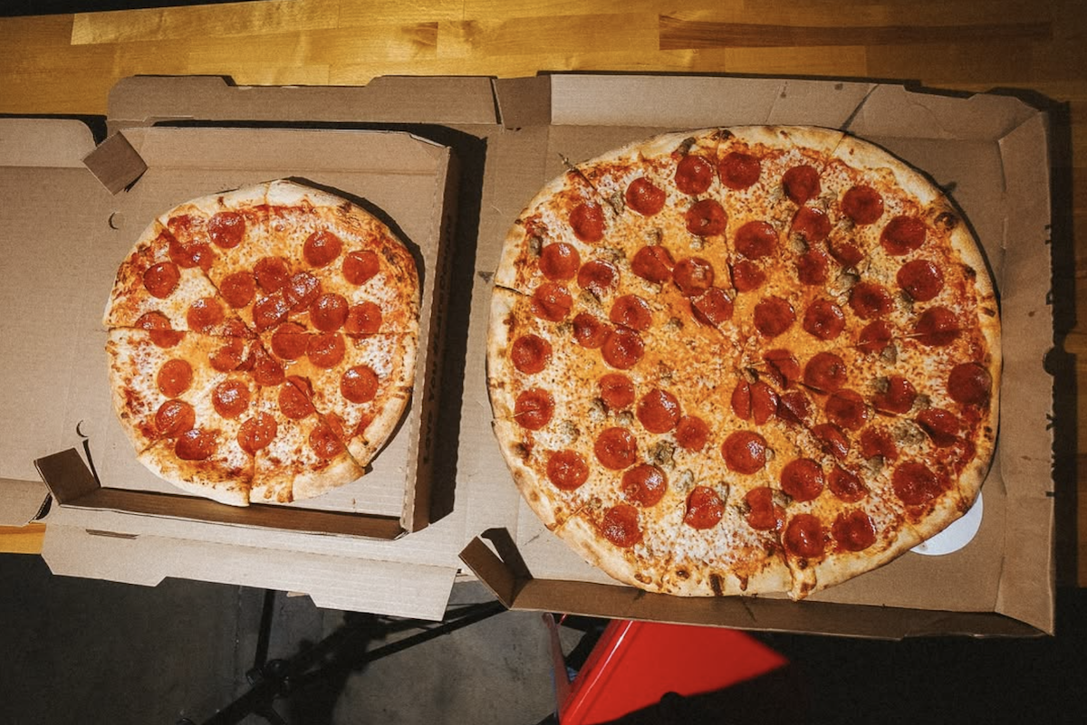 Two pepperoni pizzas side by side. The one on the left is a 14" pizza, the one on the right is an 18" pizza and dwarfs the other.
