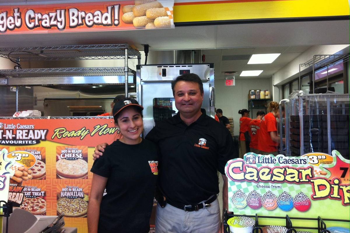 A father-daughter duo pose behind the counter at a Little Caesars store in Barrie, Ontario.
