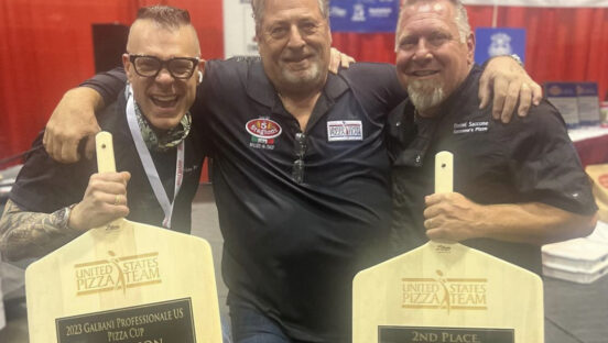 This photo shows two of the winners of last year's Galbani Professionale Pizza Cup holding their trophy peels along with a judge standing between them.