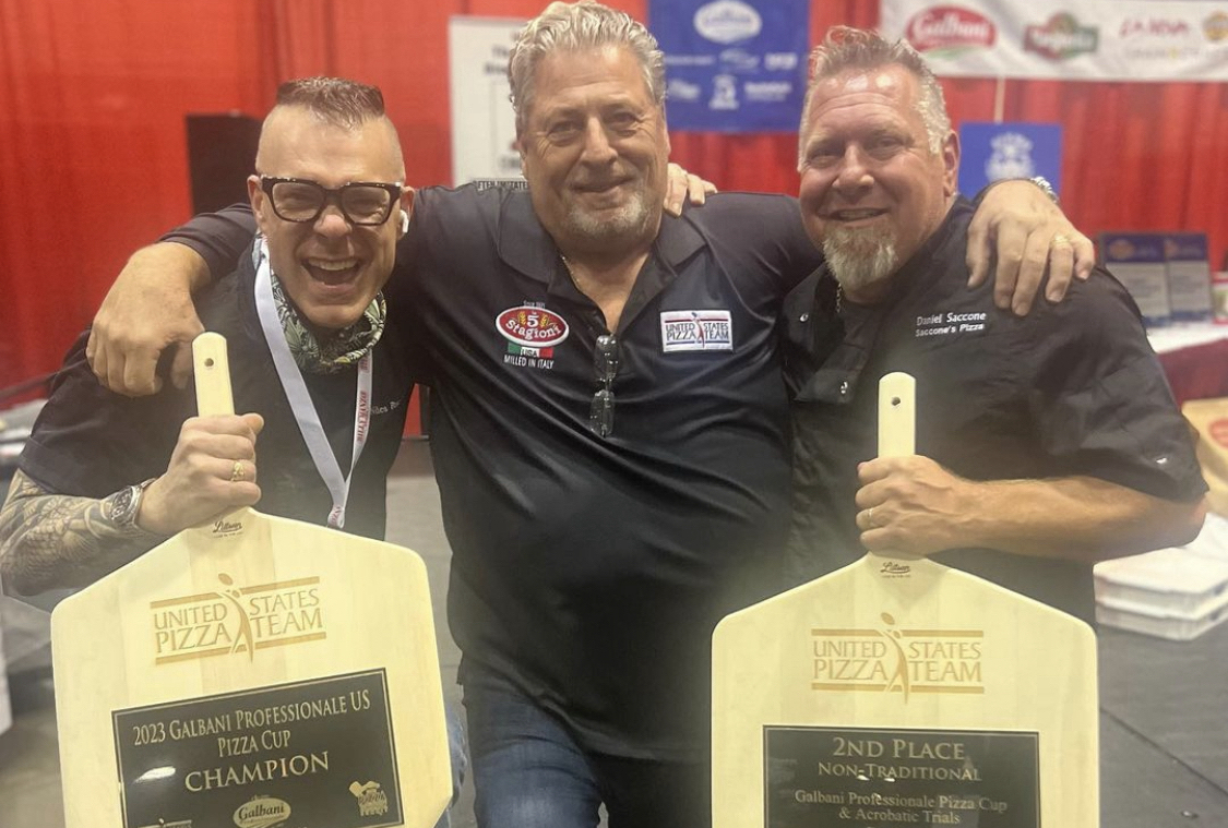 This photo shows two of the winners of last year's Galbani Professionale Pizza Cup holding their trophy peels along with a judge standing between them.