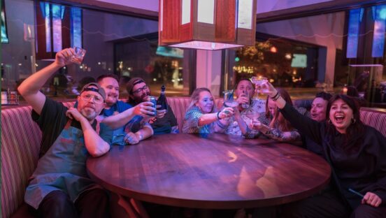 This photo shows a group of happy people making a toast with their drinks at Mothership Pizza Paradise.