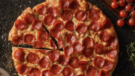 A fresh pepperoni pizza with one slice partially removed on a black background.