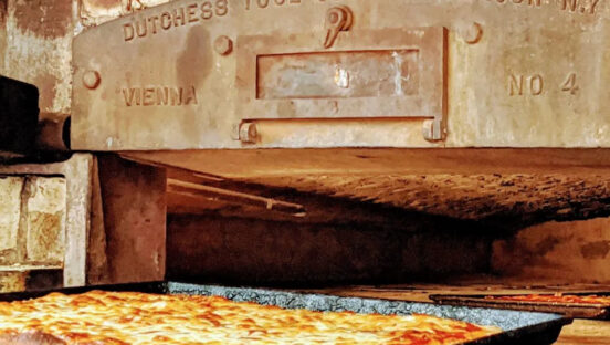 This photo shows a cheese pizza in a pan placed before the 100-year-old brick oven at Santillo's.