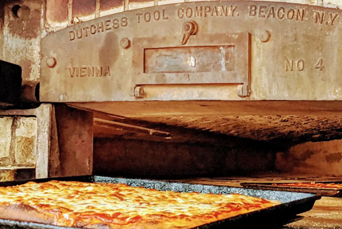 This photo shows a cheese pizza in a pan placed before the 100-year-old brick oven at Santillo's.