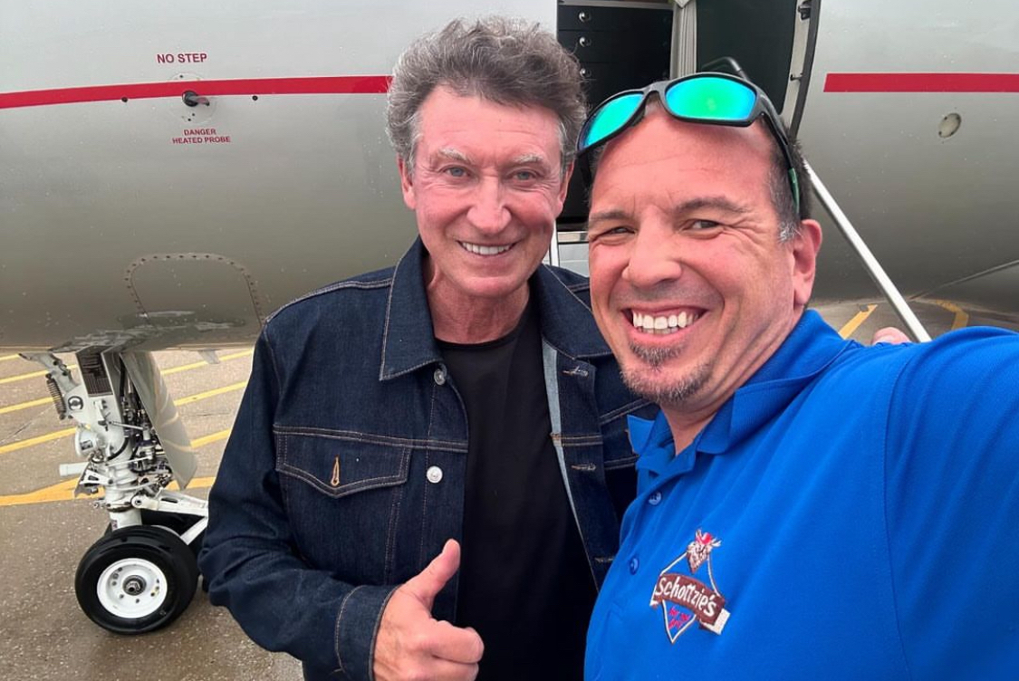 This photo shows Wayne Gretzky, smiling and giving a thumbs-up, posing in front of his private jet with the owner of Schottzie's.