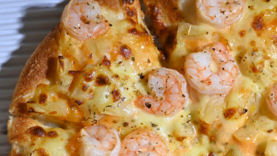 This photo shows a pizza topped with cheese, shrimp and pineapple dices.