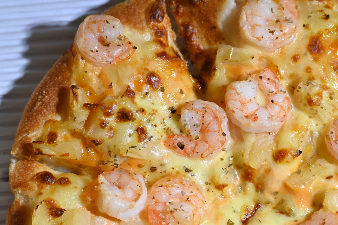 This photo shows a pizza topped with cheese, shrimp and pineapple dices.