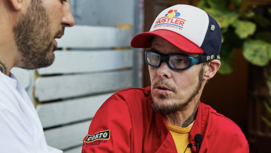 Auggie Russo, with a hat and Rex Specs, speaks to another pizzaiolo.