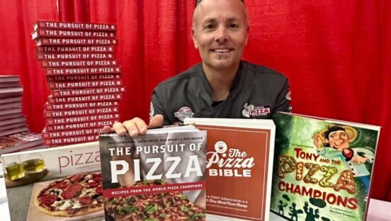 This photo shows Tony Gemignani sitting at a table with several of his books.