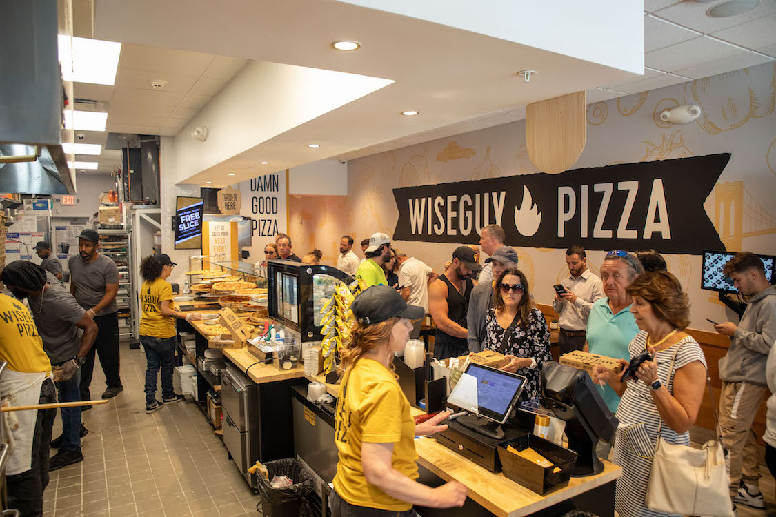 This photo shows a crowd of customers at a Wiseguy Pizza location.
