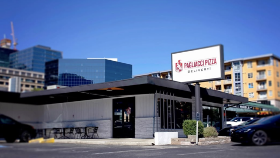 The outside of a Pagliacci Pizza location, with large buildings in the background.