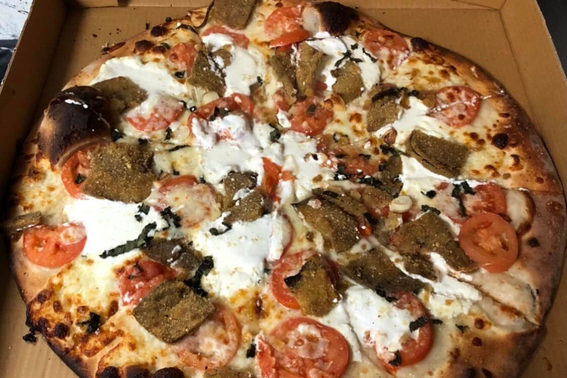 This photo shows a Mr. B's pizza topped with tomatoes, ricotta, eggplant and garlic.