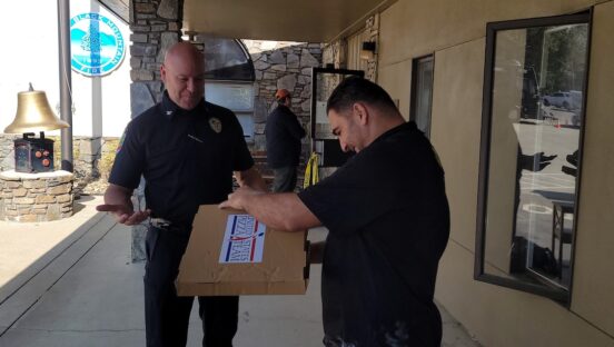 This photo shows a police officer getting ready to take a boxed pizza from a U.S. Pizza Team member.