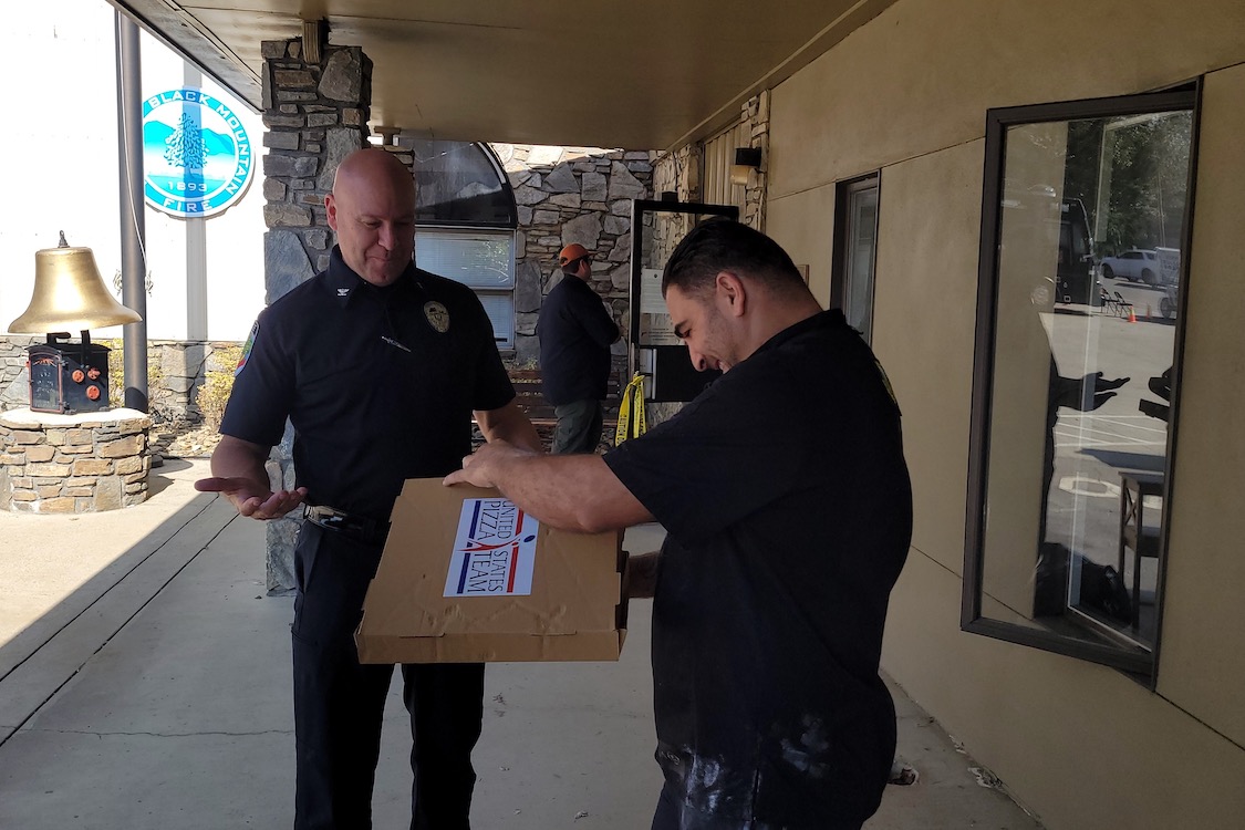 This photo shows a police officer getting ready to take a boxed pizza from a U.S. Pizza Team member.