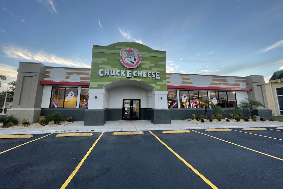 This photo shows the exterior of a Chuck E. Cheese restaurant, with the parking lot in front and a blue sky in the background.