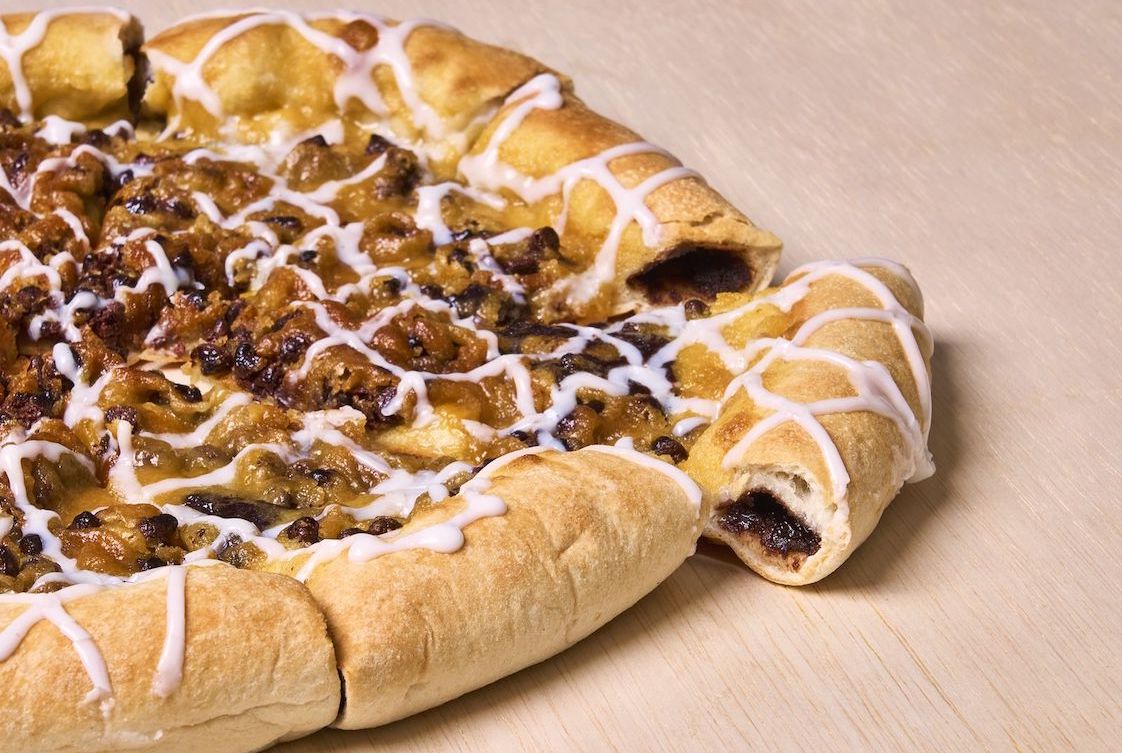 This photo shows a dessert pizza with a piece of crust pulled out to reveal the chocolate fudge stuffed inside it.