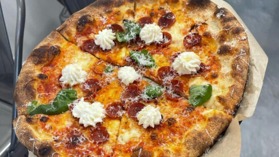 This photo shows a pizza topped with ricotta flowers, pepperoni and basil leaves.