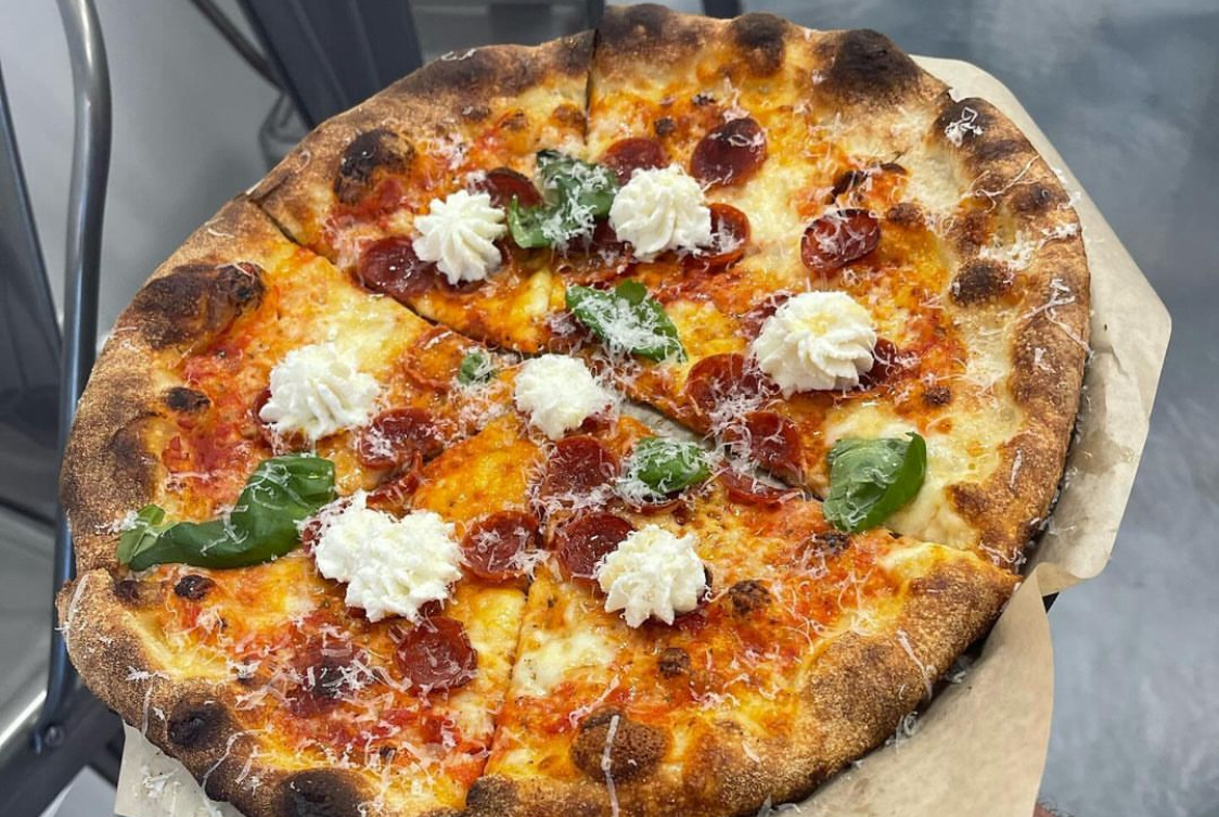 This photo shows a pizza topped with ricotta flowers, pepperoni and basil leaves.