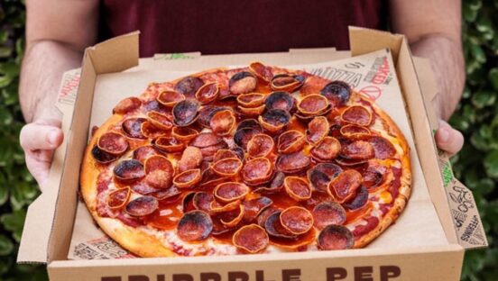 This photo shows a man's hands holding a boxed pizza topped with triple pepperoni.