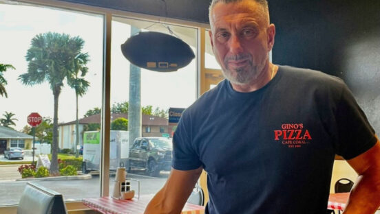 This photo shows Dino Iuliano in his restaurant, wearing a dark blue t-shirt with the Gino's Pizza logo.