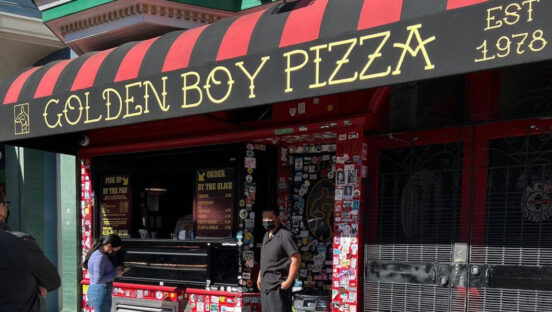 This photo shows a man standing in front of the Golden Boy Pizza entrance in San Francisco.