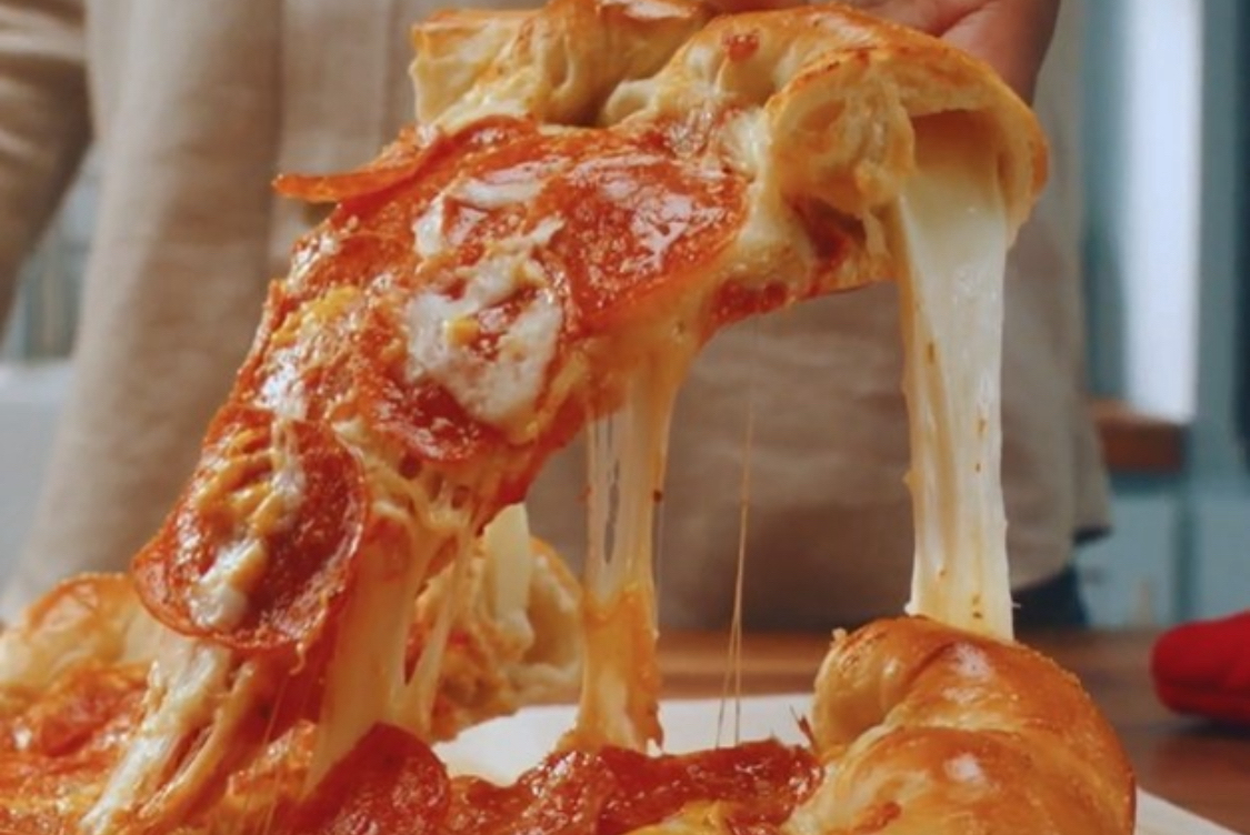 This photo shows a slice being removed from a stuffed-crust pizza with a great cheese pull.
